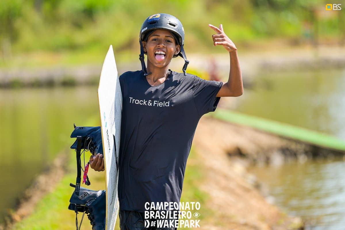 Atleta sorrindo com a prancha de wakeboard debaixo do braço